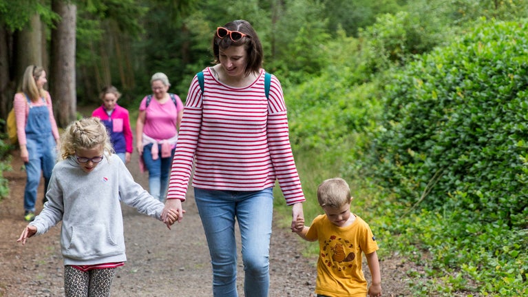 A group visiting Cragside. 1 adult and 2 children in the foreground. They are walking along a path at Cragside.